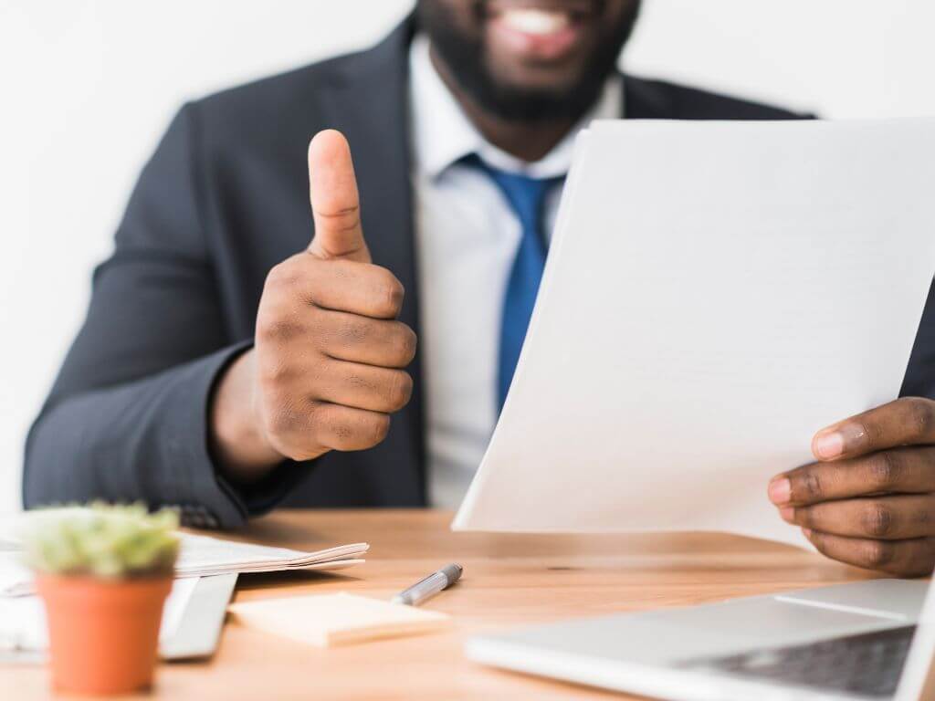 A businessman in a blue suit giving a thumbs up while holding a document.