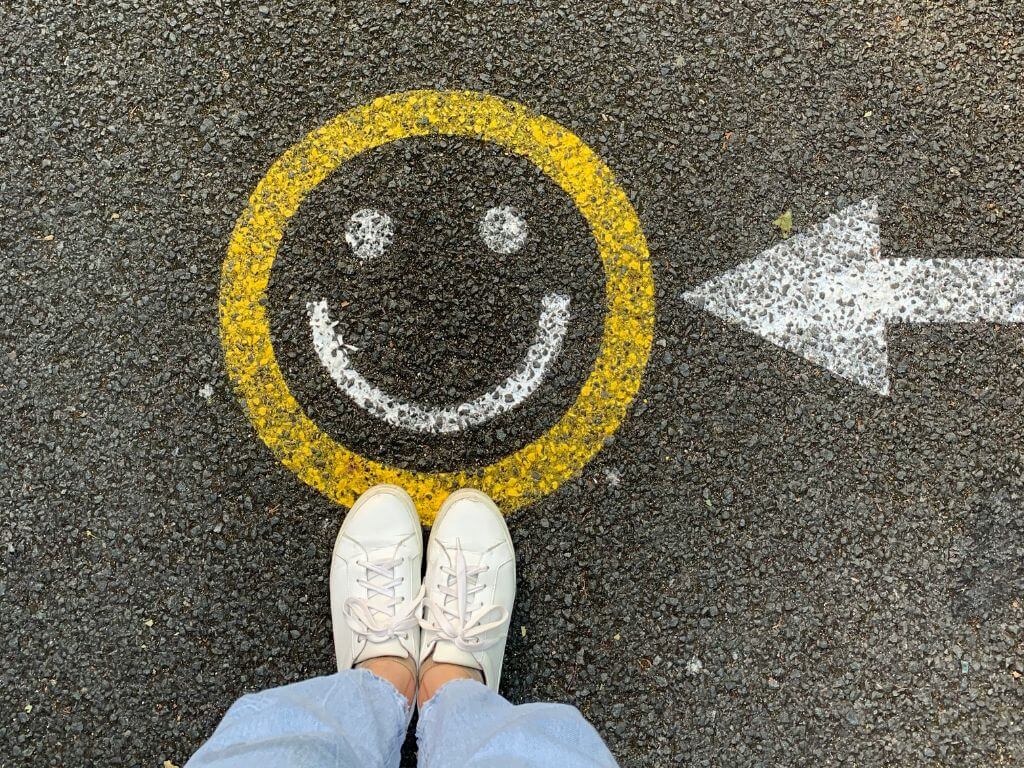 Person standing on a pavement with feet visible, next to a smiley face and an arrow pointing to the right.