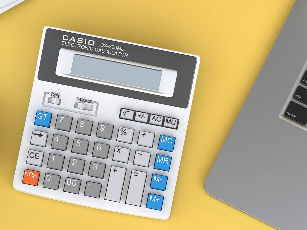 Casio electronic calculator on a yellow desk beside a laptop