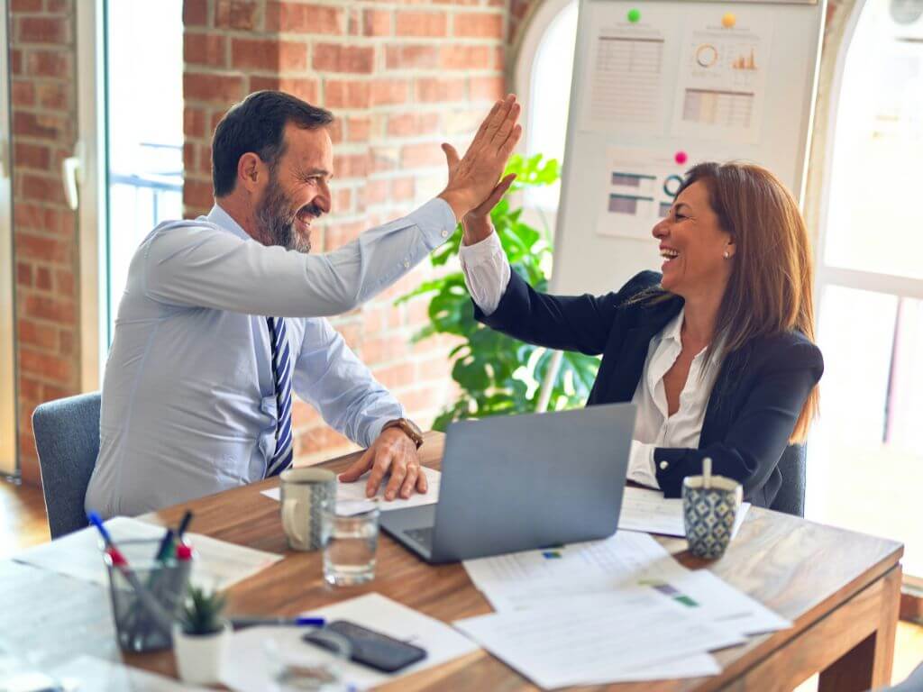 Two business colleagues smiling and giving each other a high-five in a modern office setting.