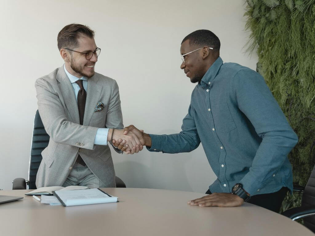 A business professional and a candidate shaking hands during an interview in a modern office setting.