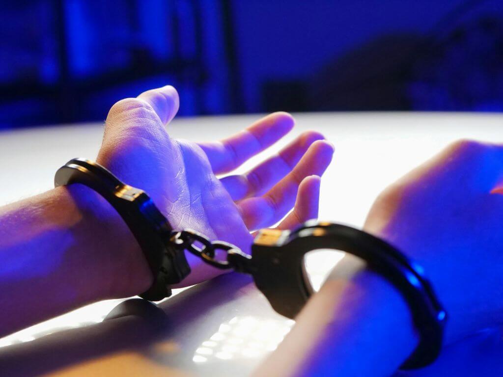 Hands in handcuffs resting on a table under blue light